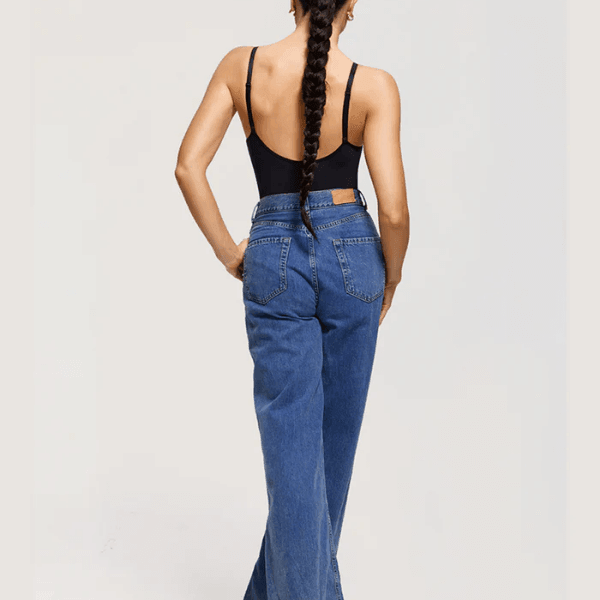 Mulher de costas usando body preto e calça jeans cintura alta, cabelo trançado longo.