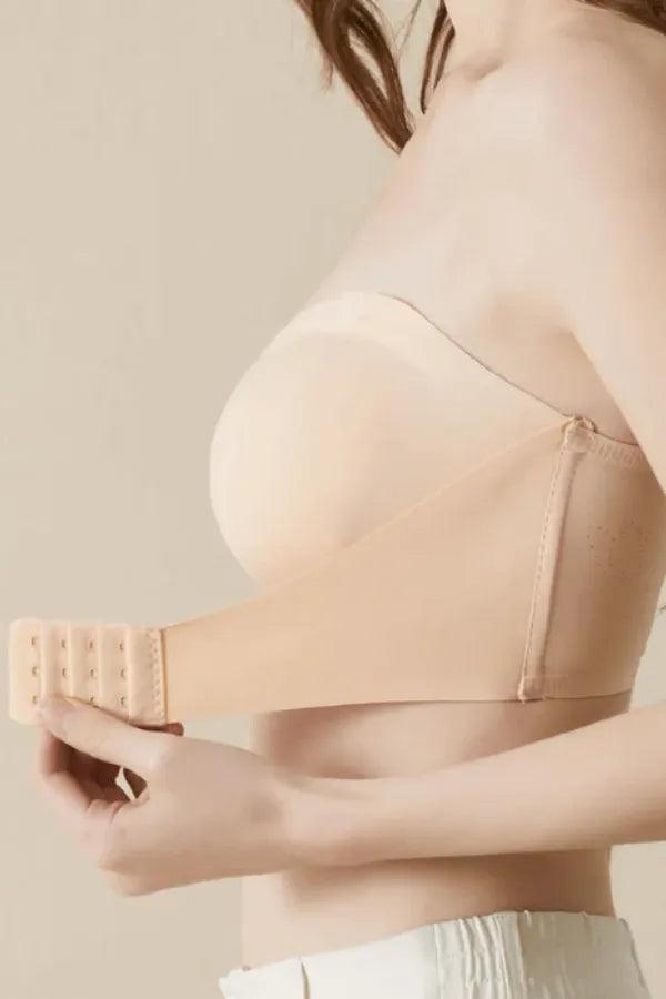 Sutiã tomara que caia nude com fecho ajustável, modelo feminino segurando a alça lateral.