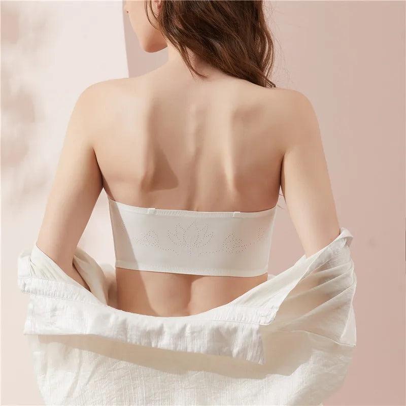 Mulher de costas usando sutiã tomara que caia branco sem alças, camisa aberta, fundo neutro.